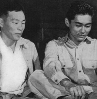 Mitsuru Doi, one of Kauai's first volunteers tries on newly issued boots while his father looks on.  [U.S. Army Signal Corps]